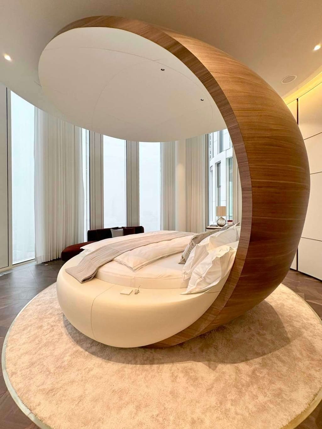 Round bed with a shell-shaped headboard and wooden frame, looking towards panoramic windows.