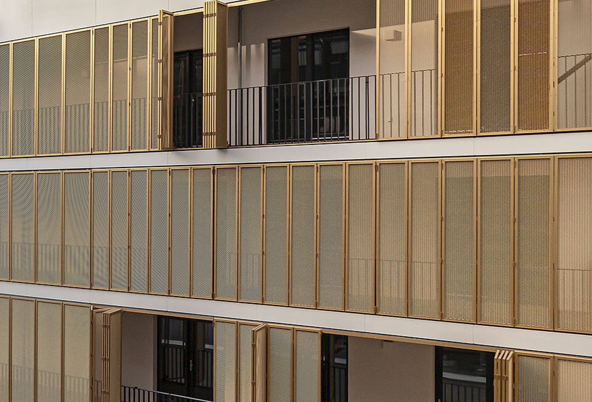 Close-up of gold-coloured folding shutters of fine perforated metal across three storeys, some elements folded open, black railings behind