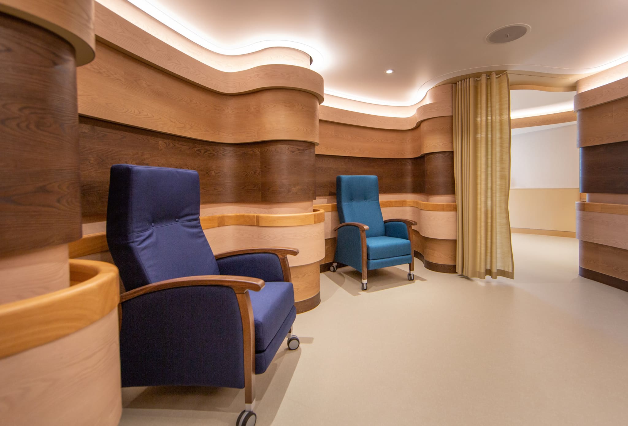 Rest alcove between wave-shaped timber walls with oak handrail, two reclining chairs in dark blue and teal, curtain at right