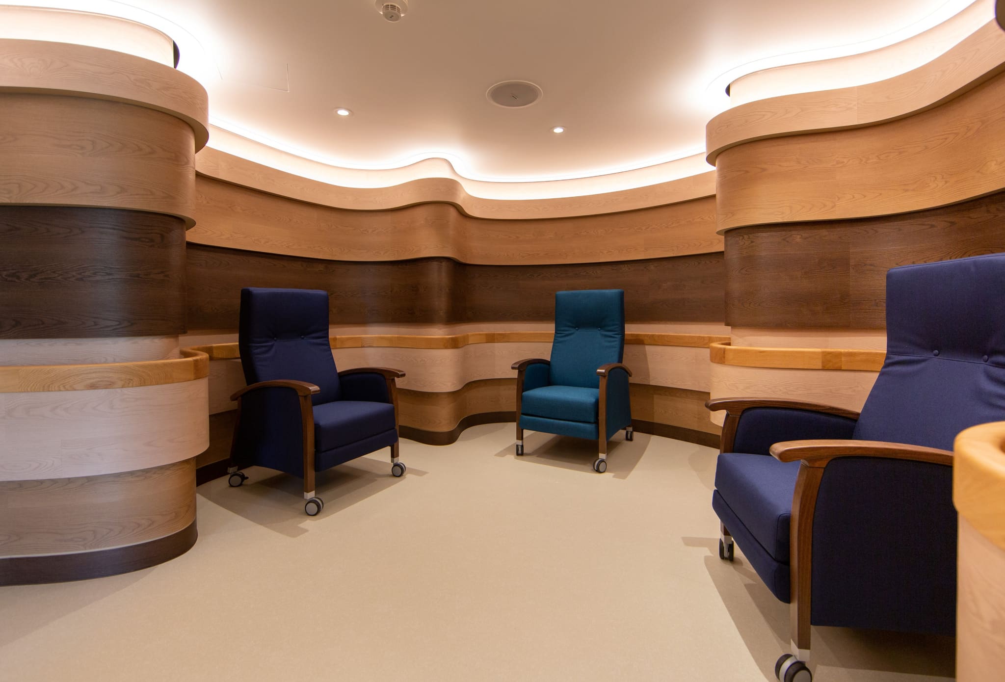 Round alcove of curved timber walls with continuous oak handrail, three reclining chairs on castors, indirect ceiling lighting