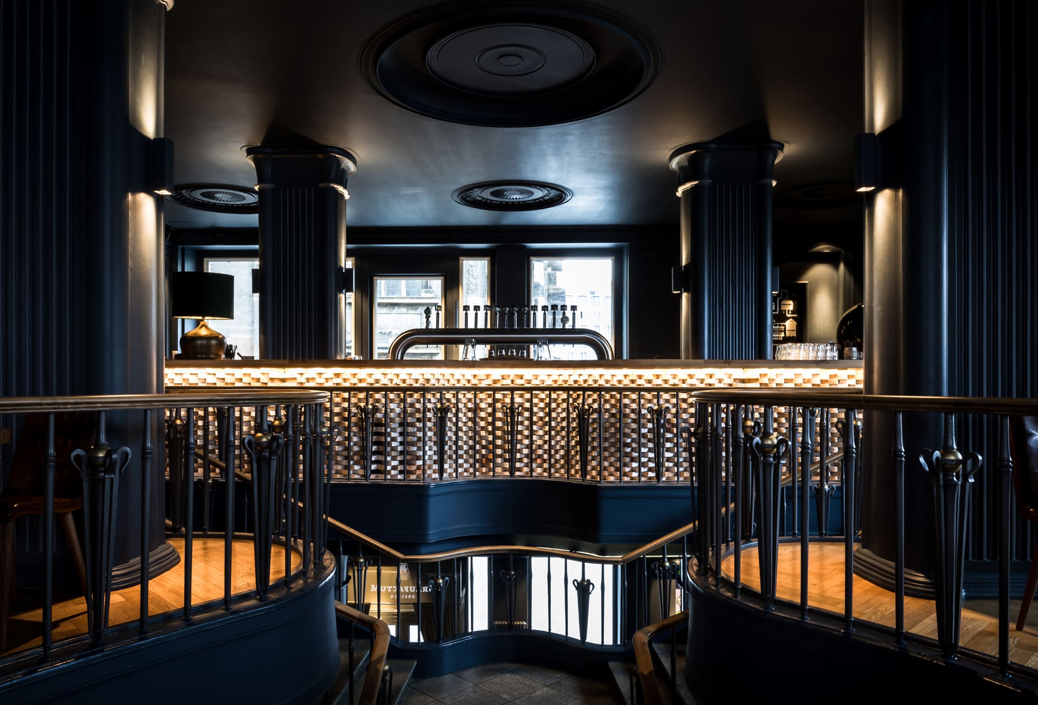 Bar counter at the head of the stairs, brick front in relief with light strip, row of taps, fluted columns