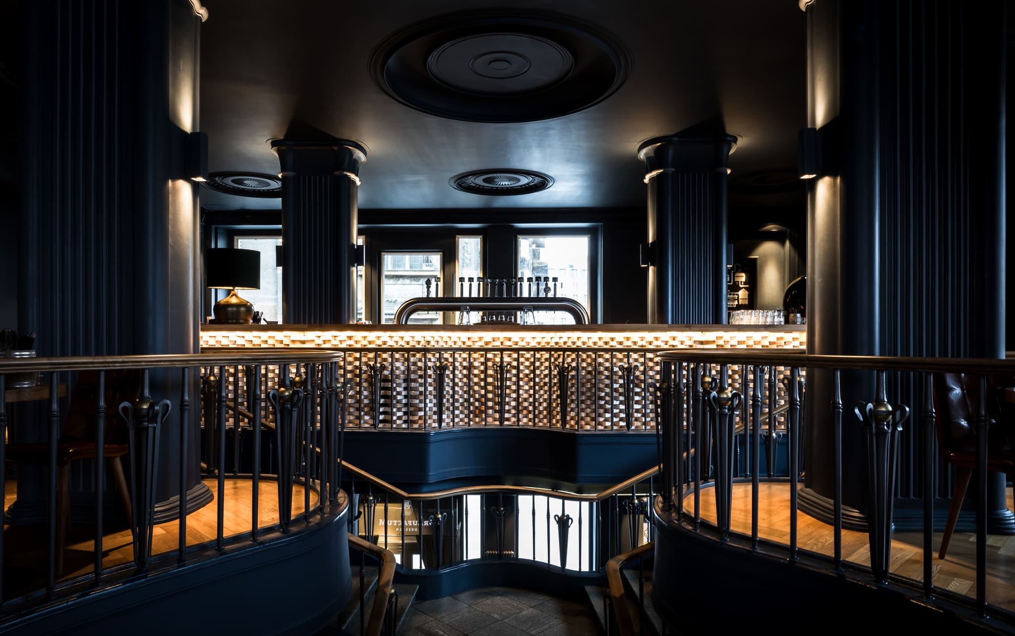 Beer taps on the brick-clad bar counter between dark blue columns, the wrought-iron railing in front