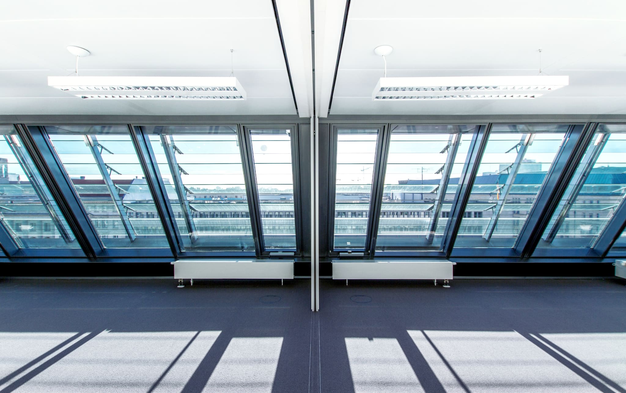 Empty training room with a sloping window front, blue carpet and two louvred luminaires above the room