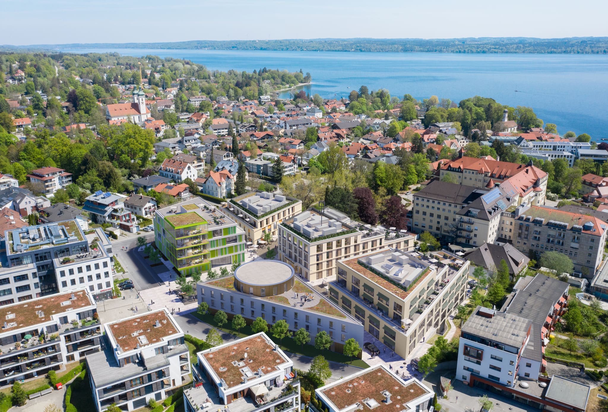 Aerial visualisation of a building ensemble with green roofs and a green-clad block, town and large lake behind