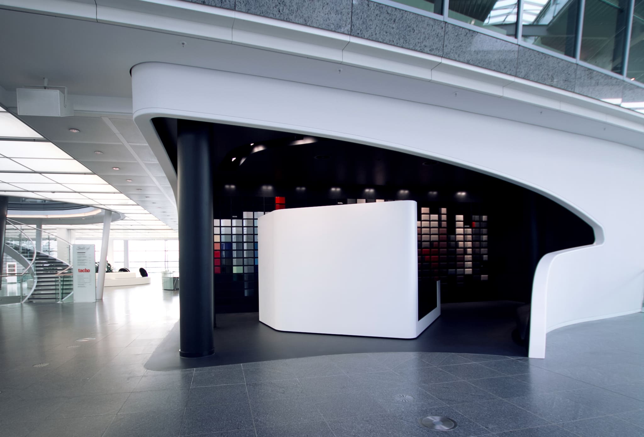 Photo of a curved white gallery edge above a dark room with sample wall, black column and granite floor