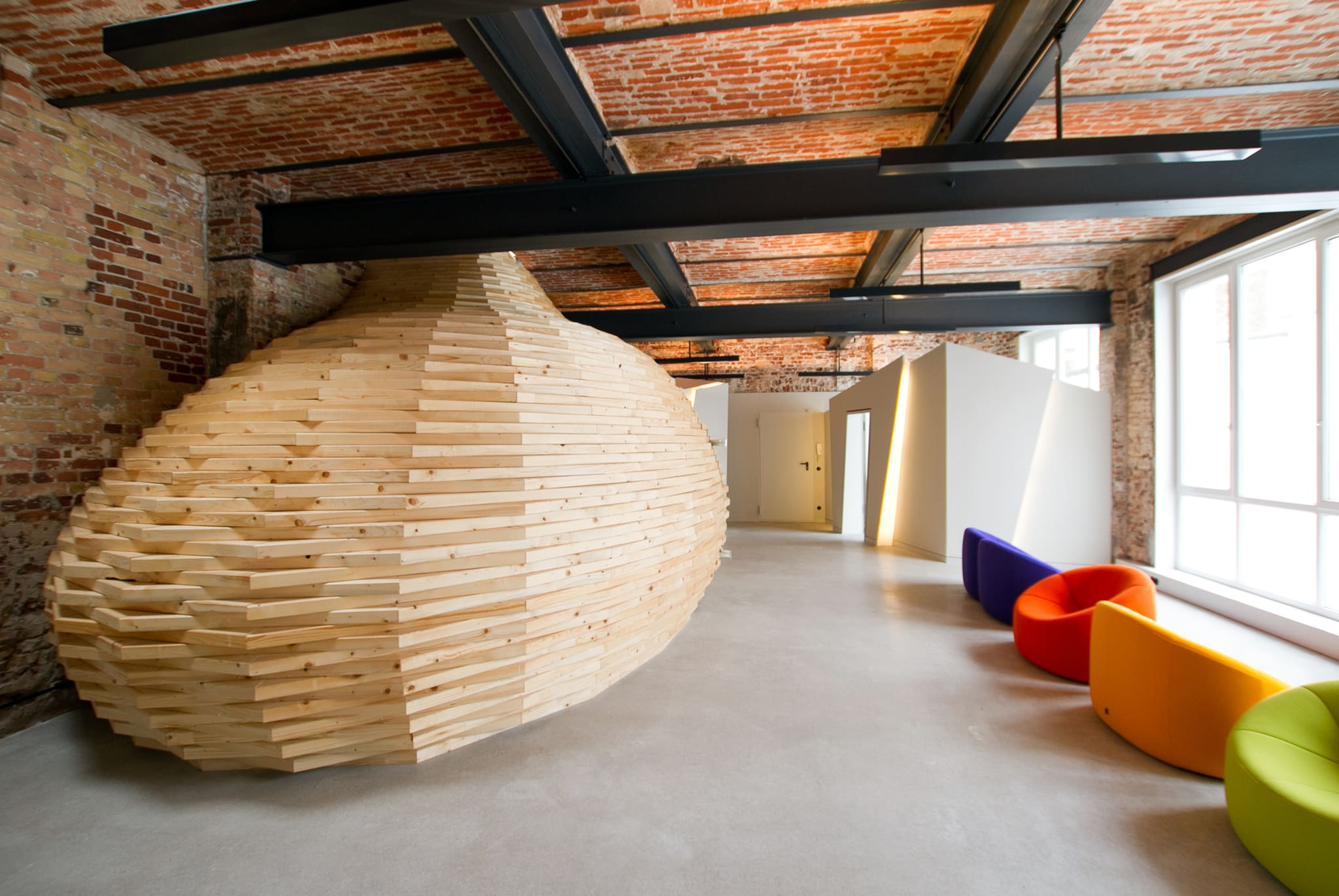 The timber cocoon in the loft beneath steel beams and a brick vaulted ceiling, colourful seats on the right