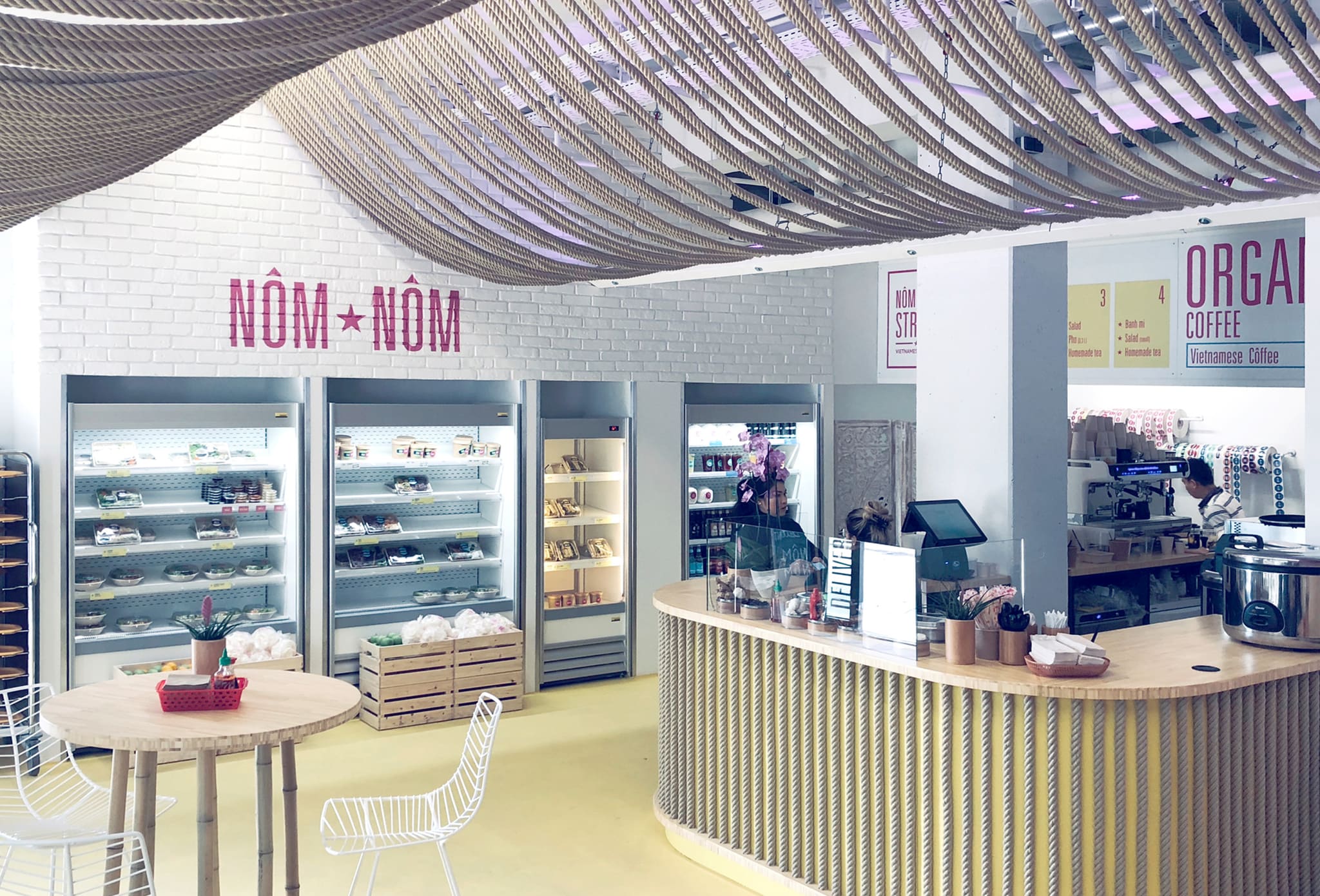 Dining space with a curved natural rope ceiling, white brick wall, chilled display units, a rope-clad counter and yellow floor