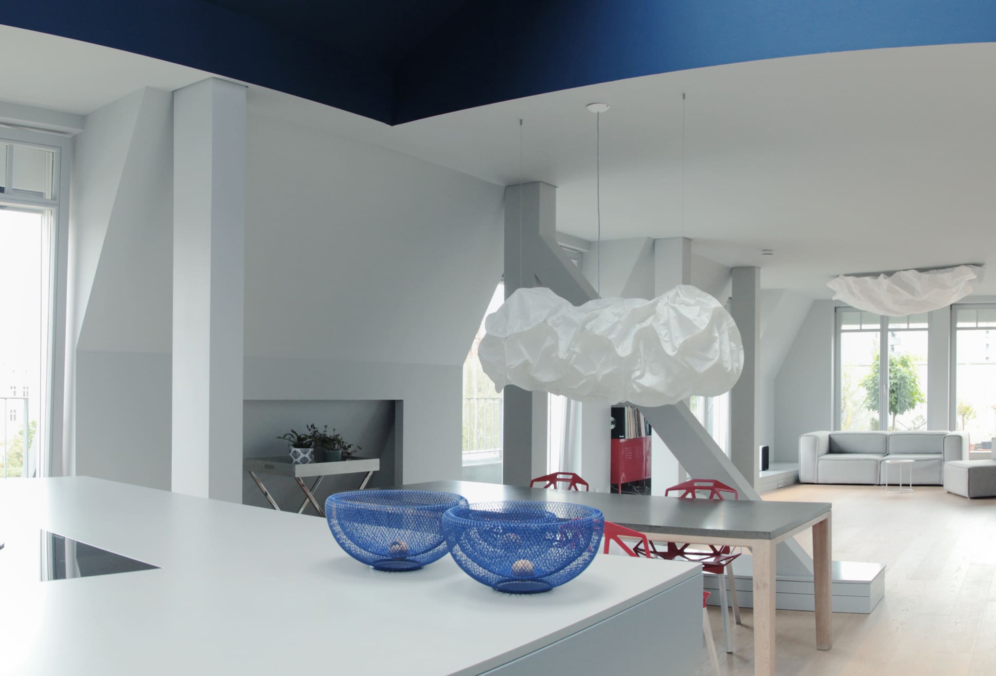View across the white kitchen worktop with two blue wire bowls to dining table and lounge, deep blue ceiling above