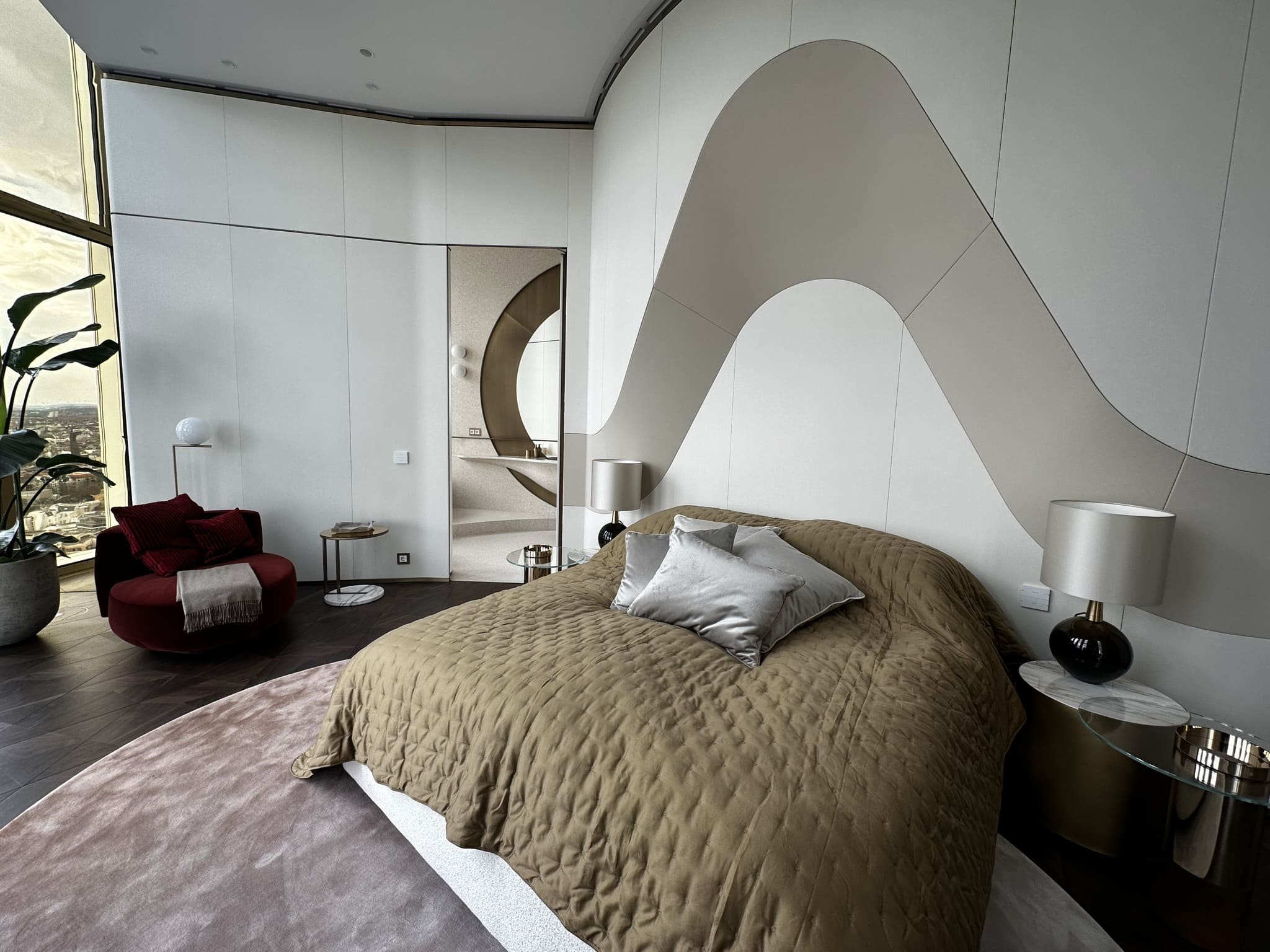 Gästezimmer mit geschwungener weißer Wandverkleidung, Bett mit goldener Tagesdecke und Leuchten