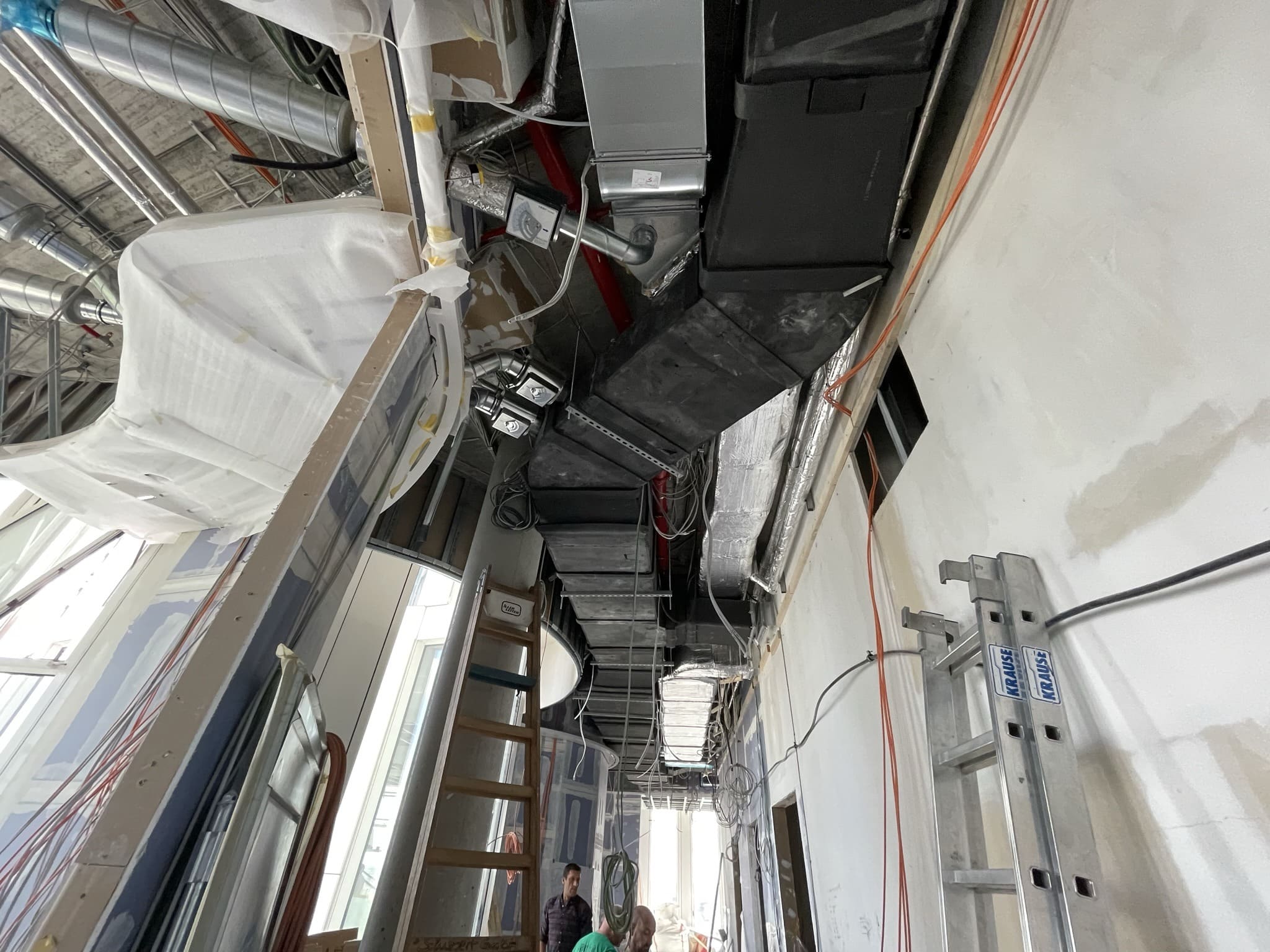 Lüftungskanäle und Leitungen über der offenen Decke im Rohbau, davor eine Leiter