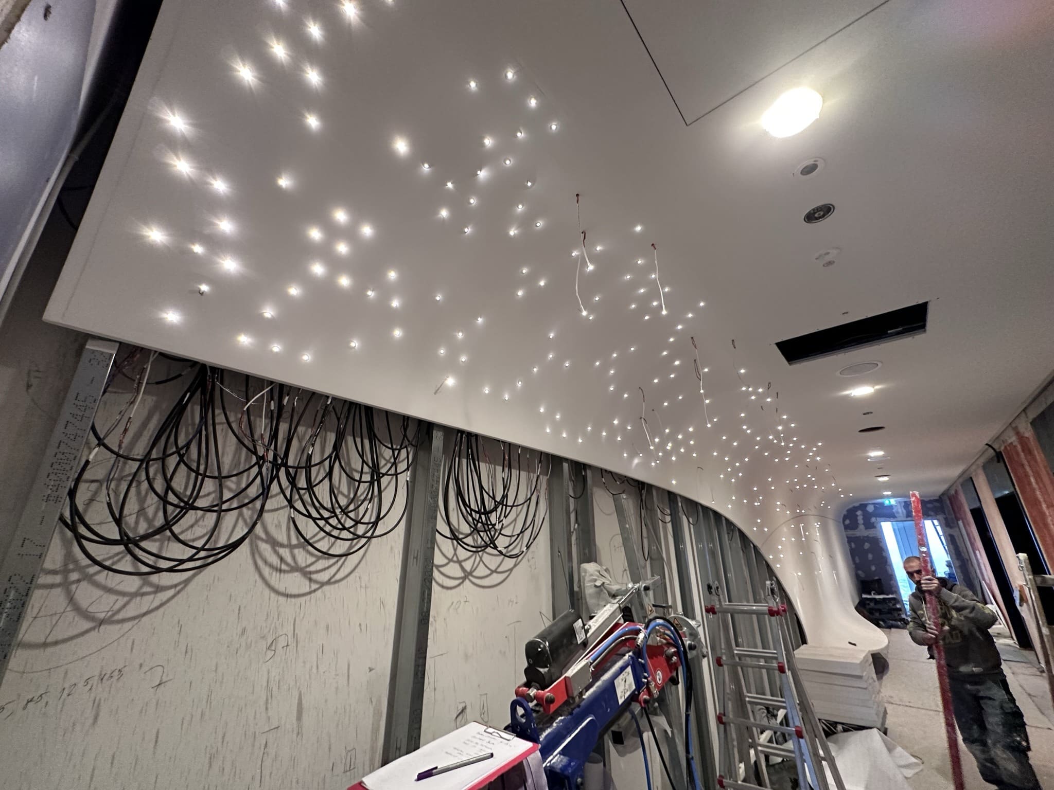 Hunderte Lichtpunkte in der geschwungenen Lobbydecke, darunter Kabelschlaufen auf der Baustelle