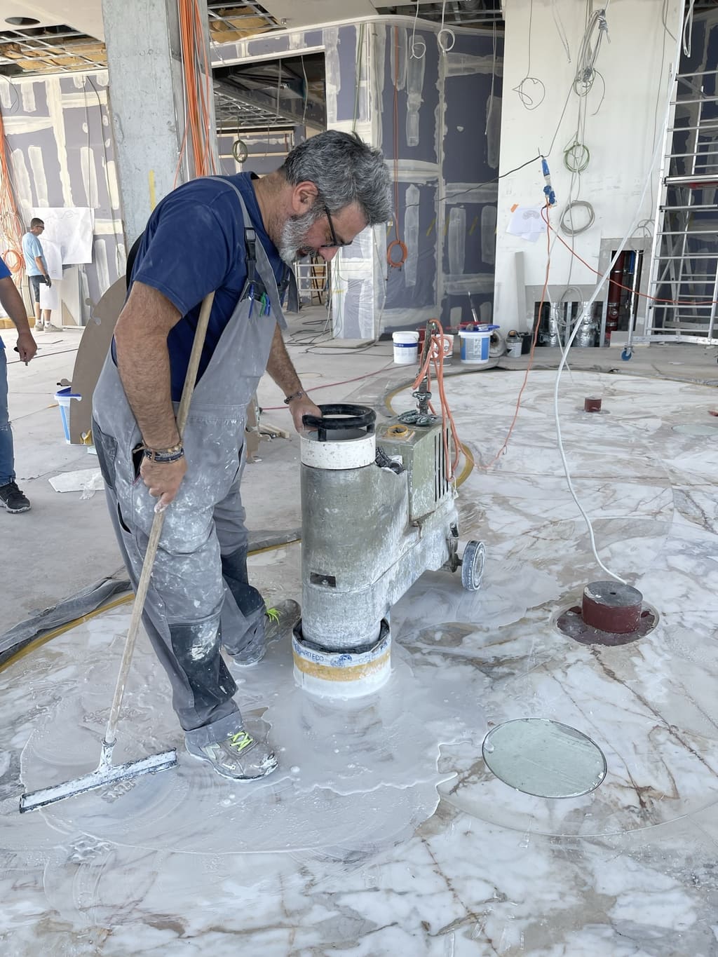 Handwerker schleift den weißen Terrazzoboden mit Messingintarsien auf der Baustelle