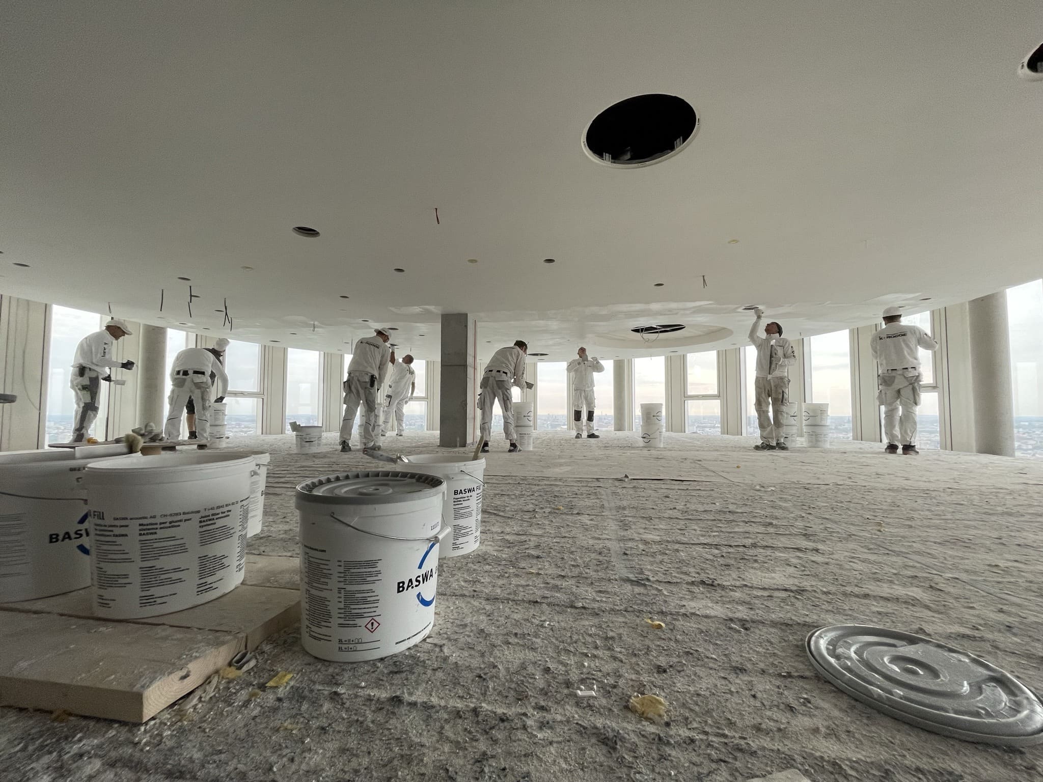 Handwerker in Weiß auf dem Flächengerüst unter der Baswa-Decke, Eimer im Vordergrund