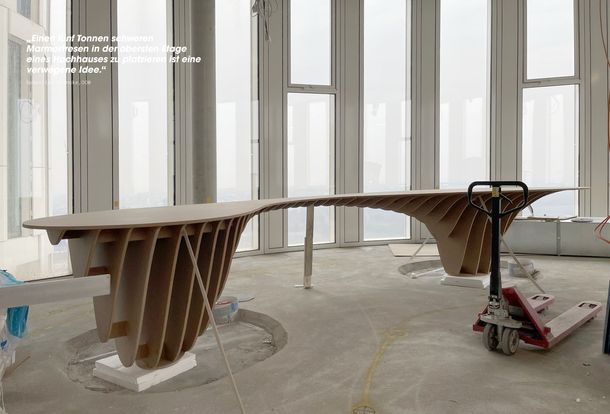 Site photo, curved rib structure of timber boards on screed in front of floor-to-ceiling windows, red pallet truck at right