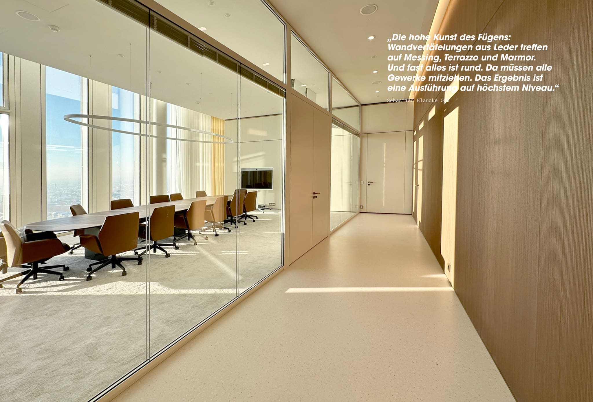 Long conference table with leather chairs and a ring light behind a glass partition, timber-panelled corridor with terrazzo floor at right