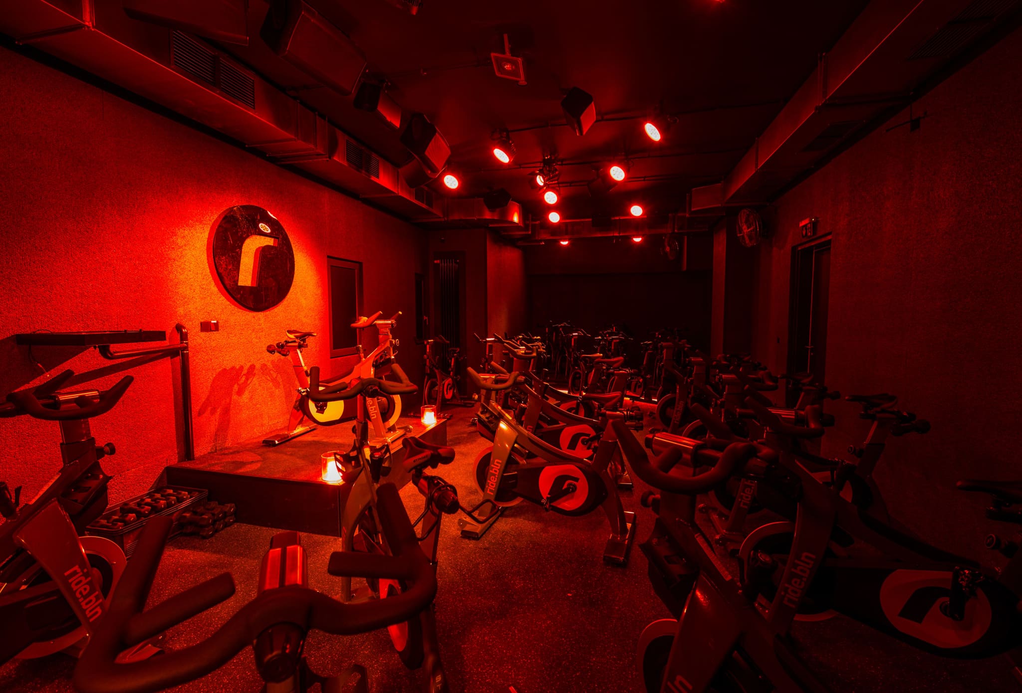 Dark training room in red light with rows of indoor bikes, podium, spotlights and loudspeakers on the ceiling