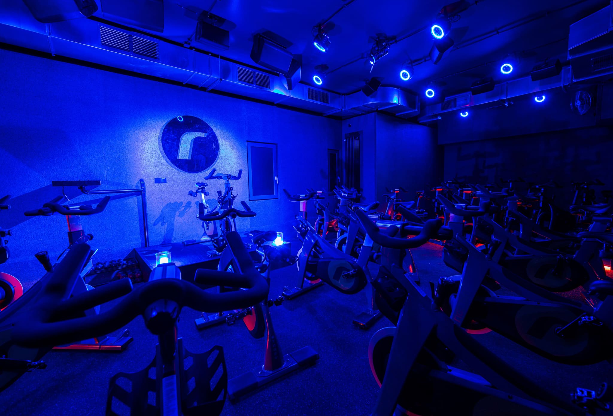 Training room in blue light with rows of indoor bikes, spotlights, ventilation outlets and rough wall lining