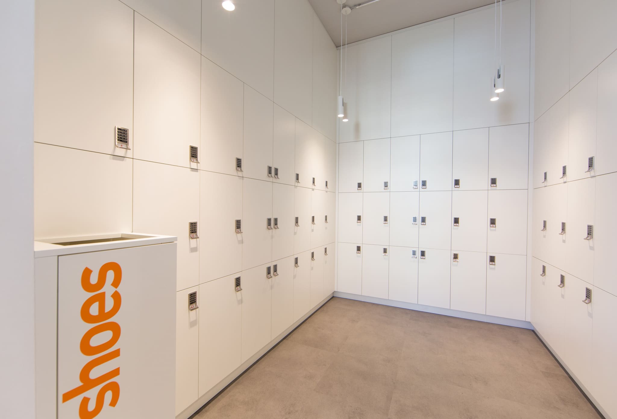 Changing room with floor-to-ceiling white lockers with code locks, two pendant lamps and pale floor covering