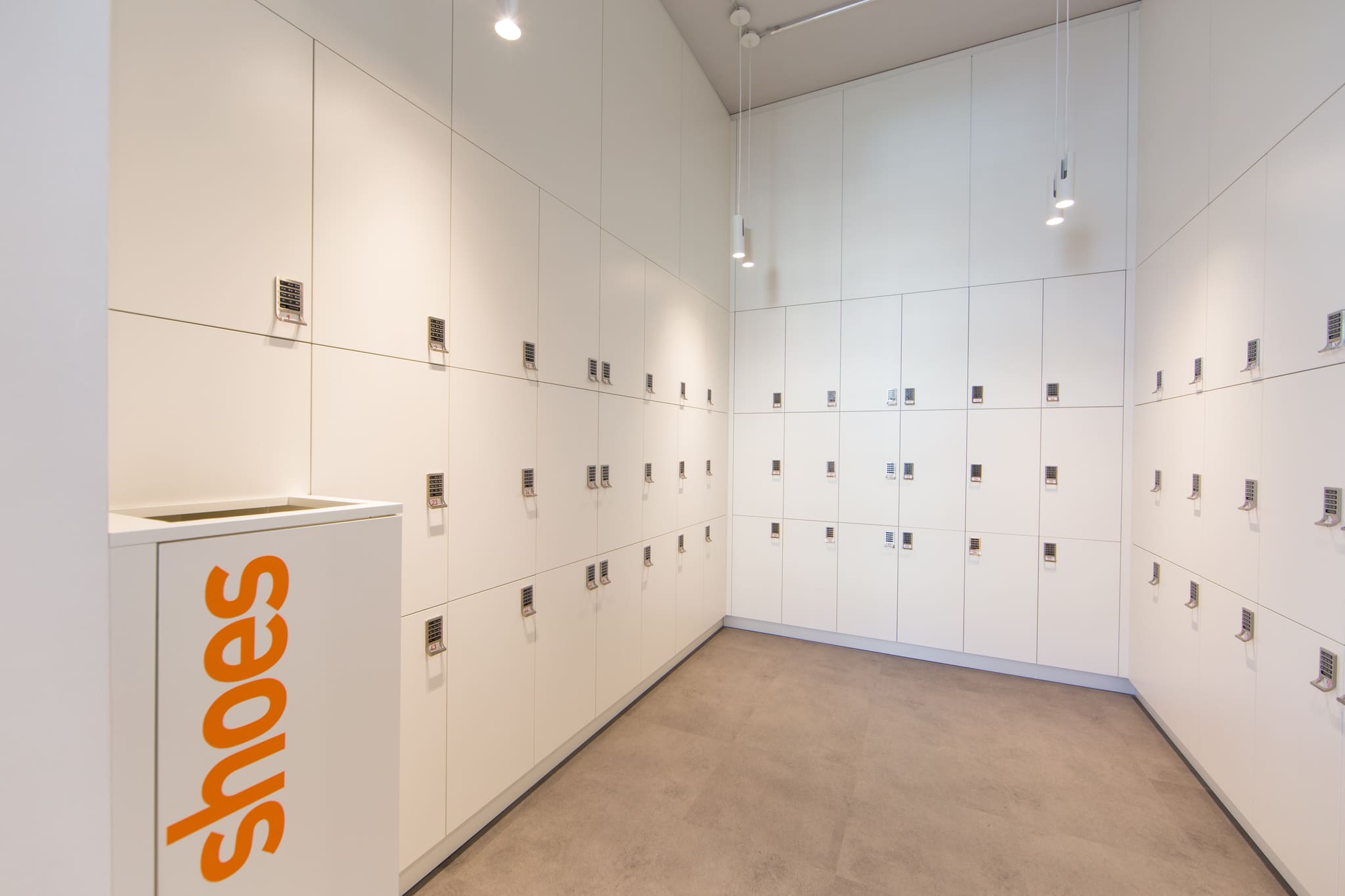 Changing room with floor-to-ceiling white lockers with code locks, two pendant lamps and pale floor covering