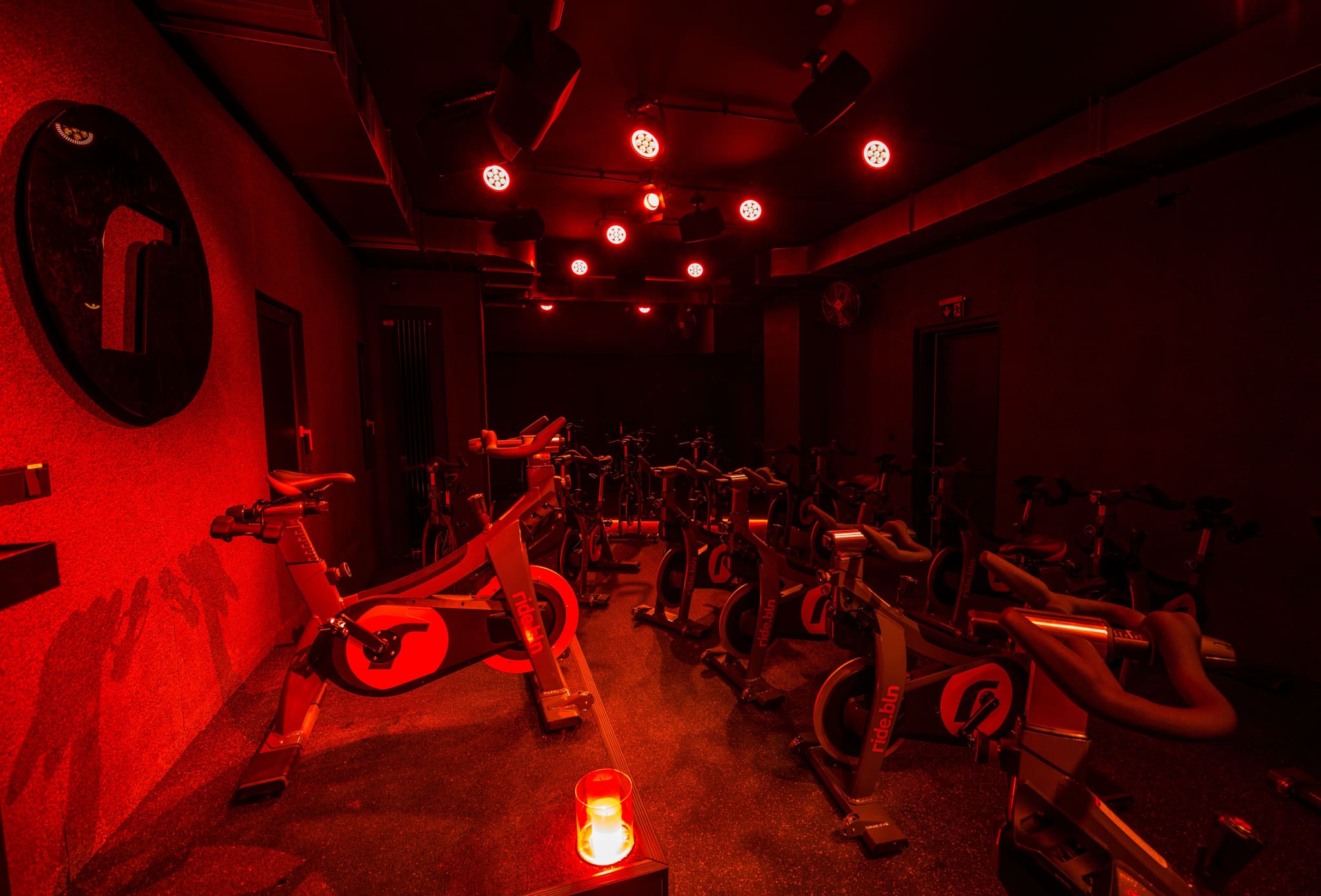 Training room in red light, view across the podium with candle to rows of indoor bikes and dark doors
