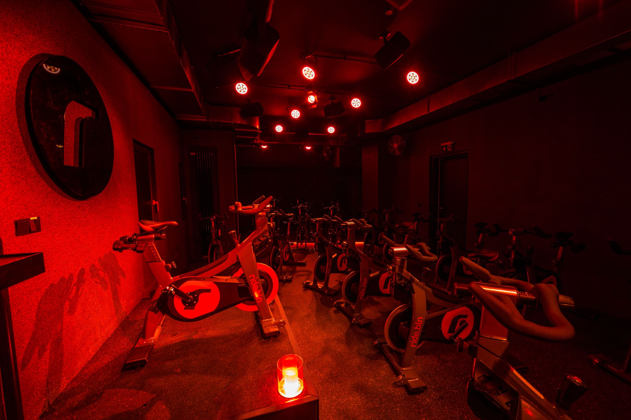 Training room in red light, view across the podium with candle to rows of indoor bikes and dark doors