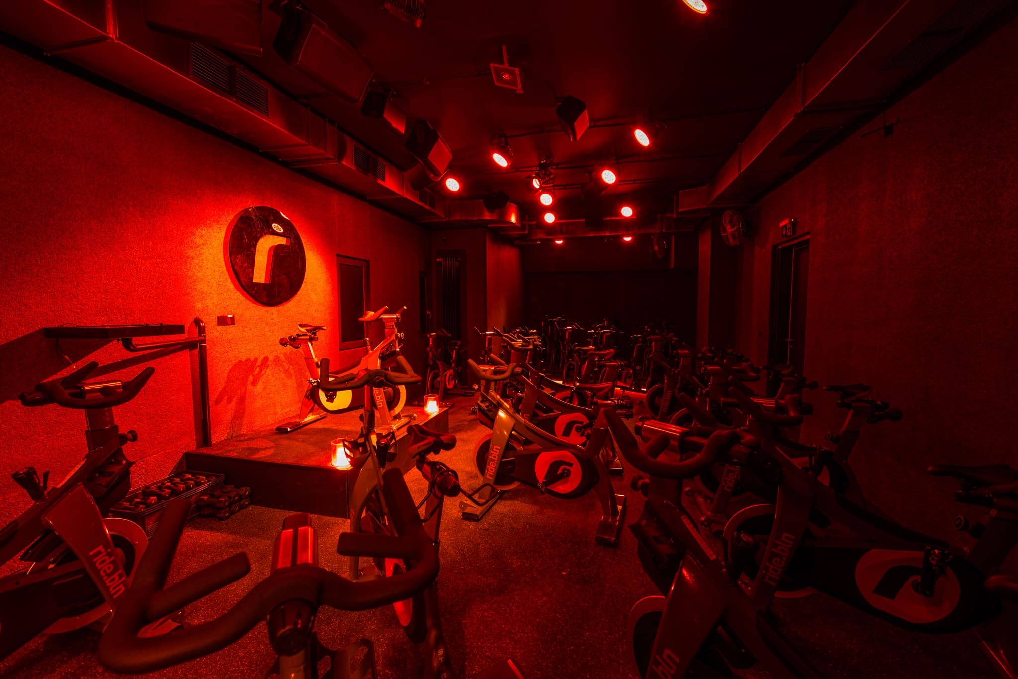 Spinning room lit in red with rows of indoor bikes and a round logo panel on the acoustic wall