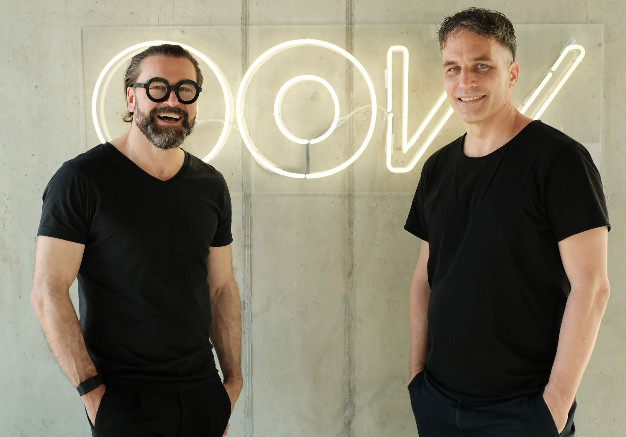 Sebastian Blancke and Mathis Malchow in front of the illuminated OOW lettering on an exposed concrete wall