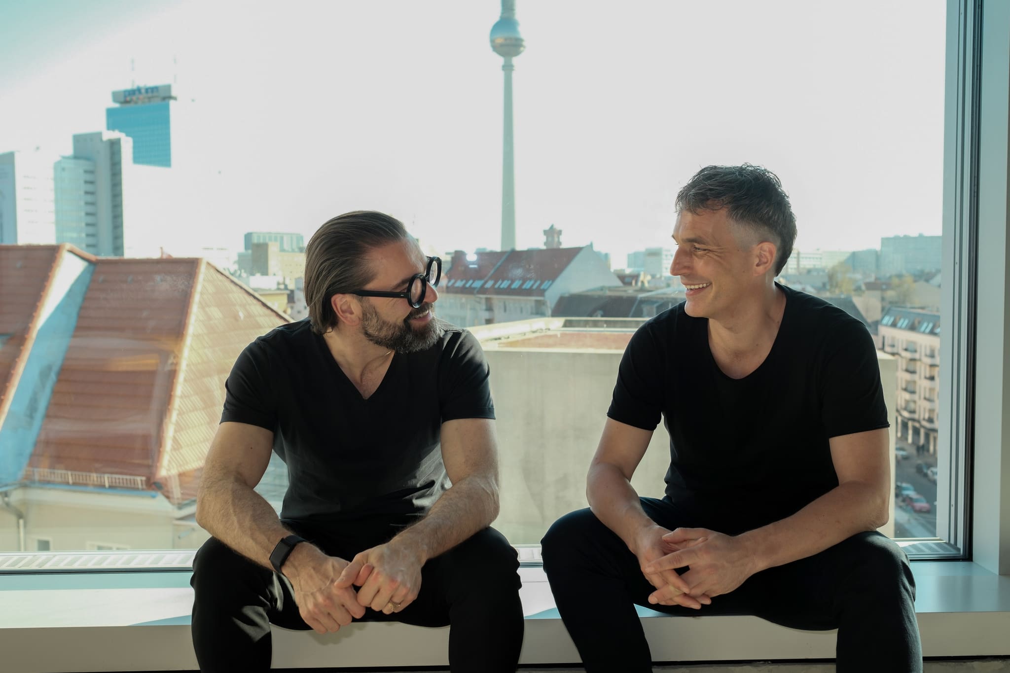 Sebastian Blancke und Mathis Malchow auf der Fensterbank im neuen Büro, dahinter der Berliner Fernsehturm